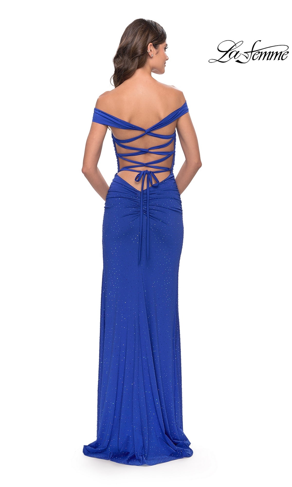 Woman wearing the La Femme Off-Shoulder Long Beaded Prom Dress 31276, featuring an off-the-shoulder neckline, lace-up open back, and a shimmering finish, stands facing away.